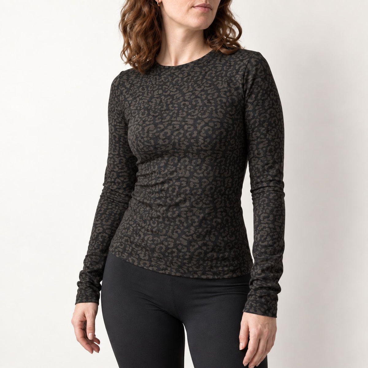 A woman wearing a fitted long-sleeve crewneck top with a dark gray and black leopard print, paired with black leggings, photographed against a plain light background.