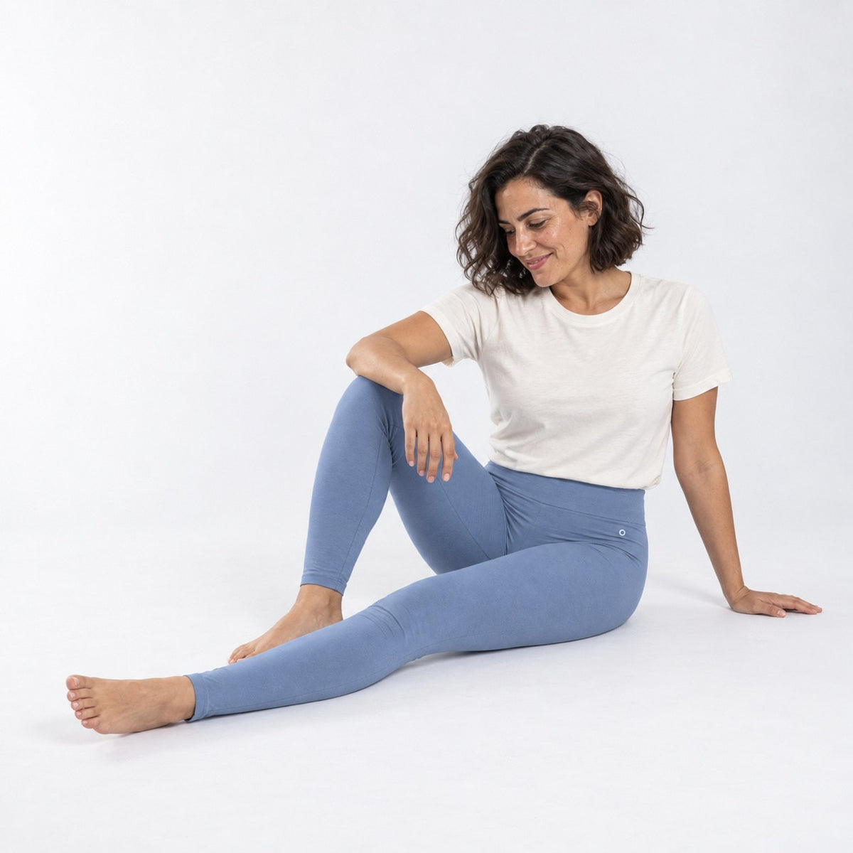 A woman sitting on a white studio floor wearing light blue organic cotton high waist leggings and a white t-shirt.