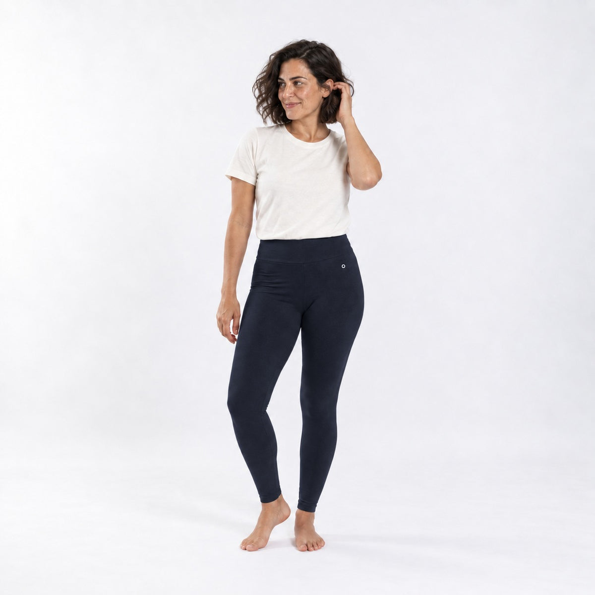 A woman modeling organic cotton high waist leggings deep blue coloand a white t-shirt against a plain white studio background.