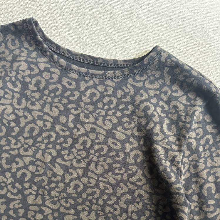 Close-up of a black leopard long sleeve top featuring a dark gray and beige leopard print pattern, laid flat on a textured off-white fabric background.