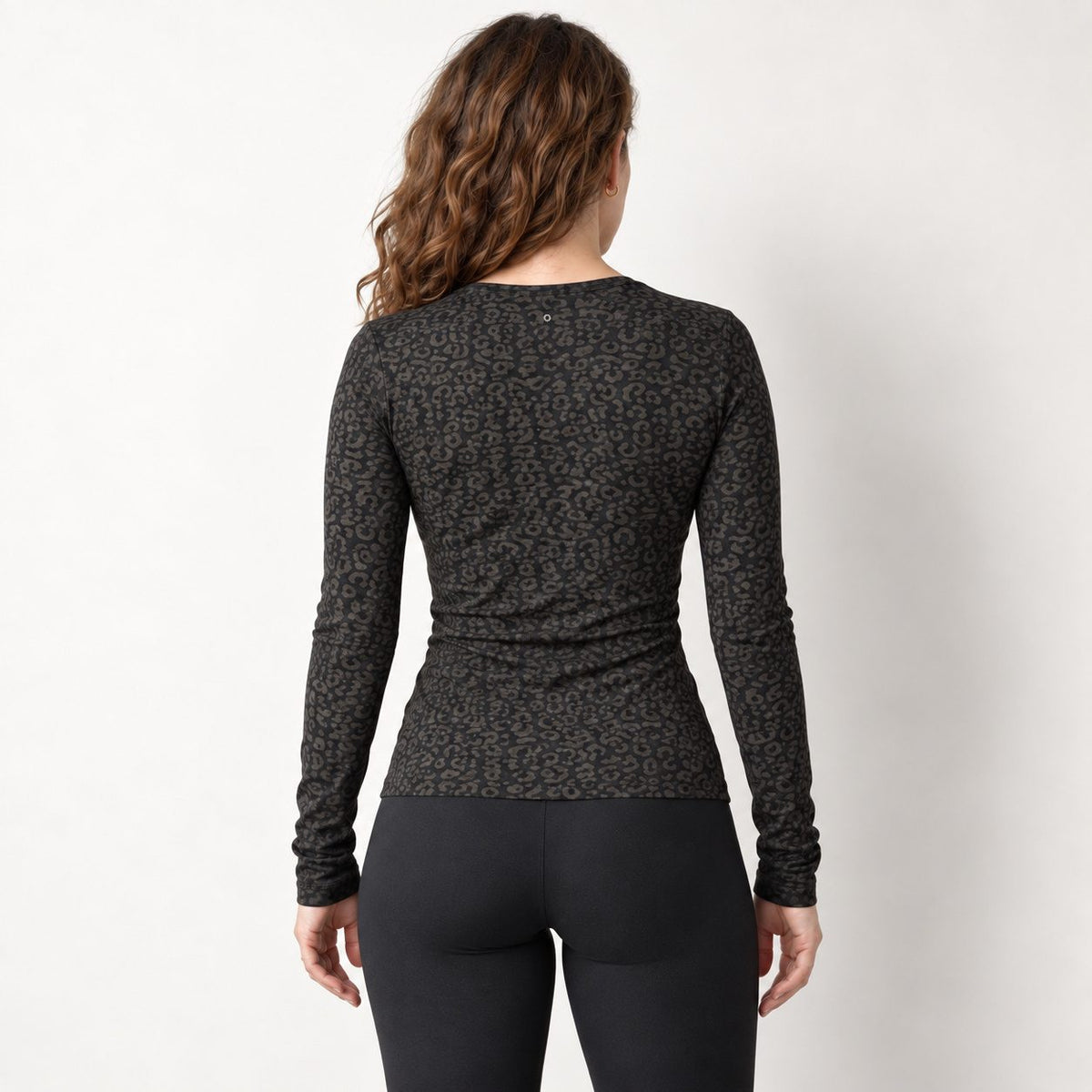 A woman viewed from the back wearing a black leopard long sleeve top with a dark brown and black leopard print, paired with black leggings, against a plain off-white studio background.