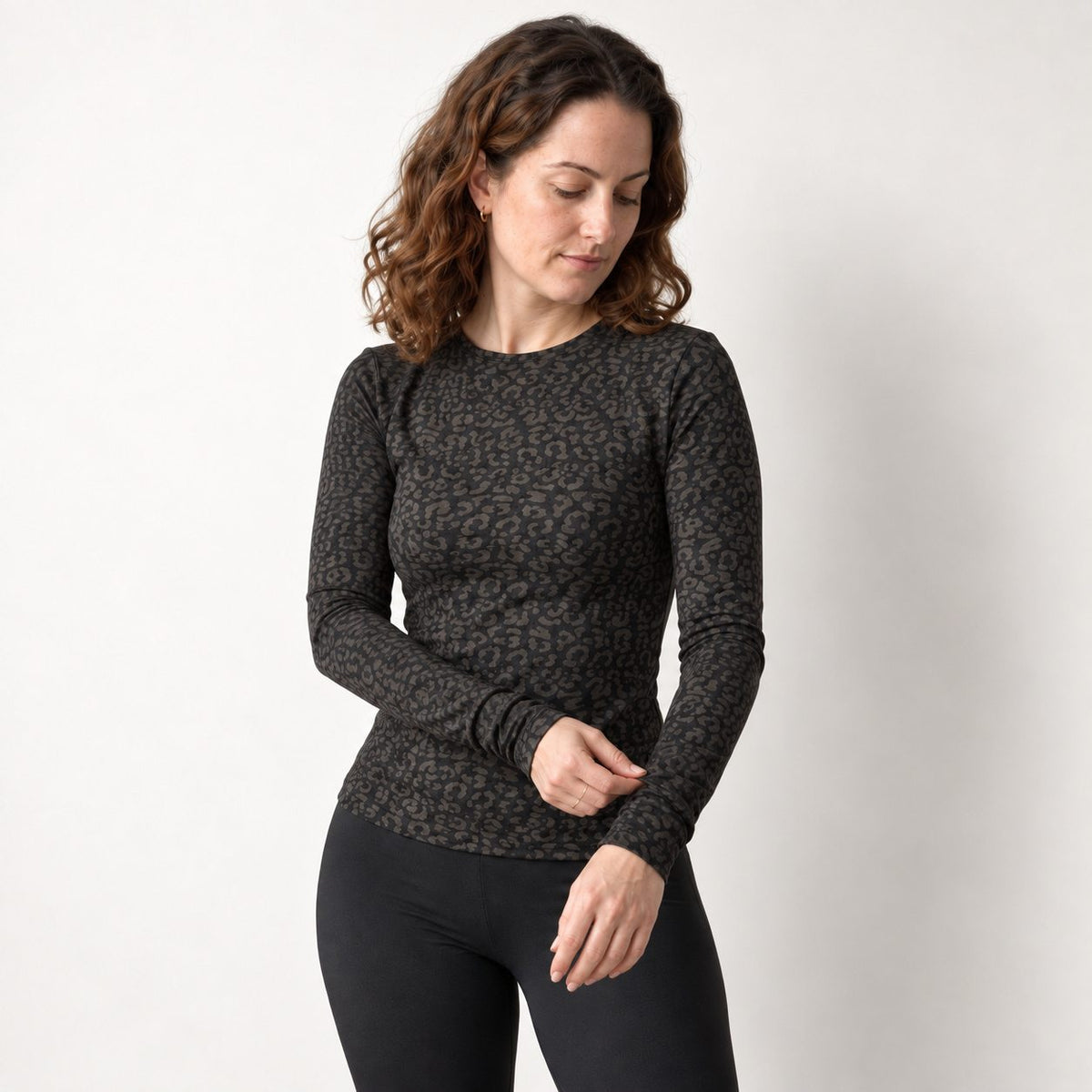 A woman wearing a fitted black leopard long sleeve top with a dark brown and black leopard print, paired with black leggings, standing against a plain light gray background.