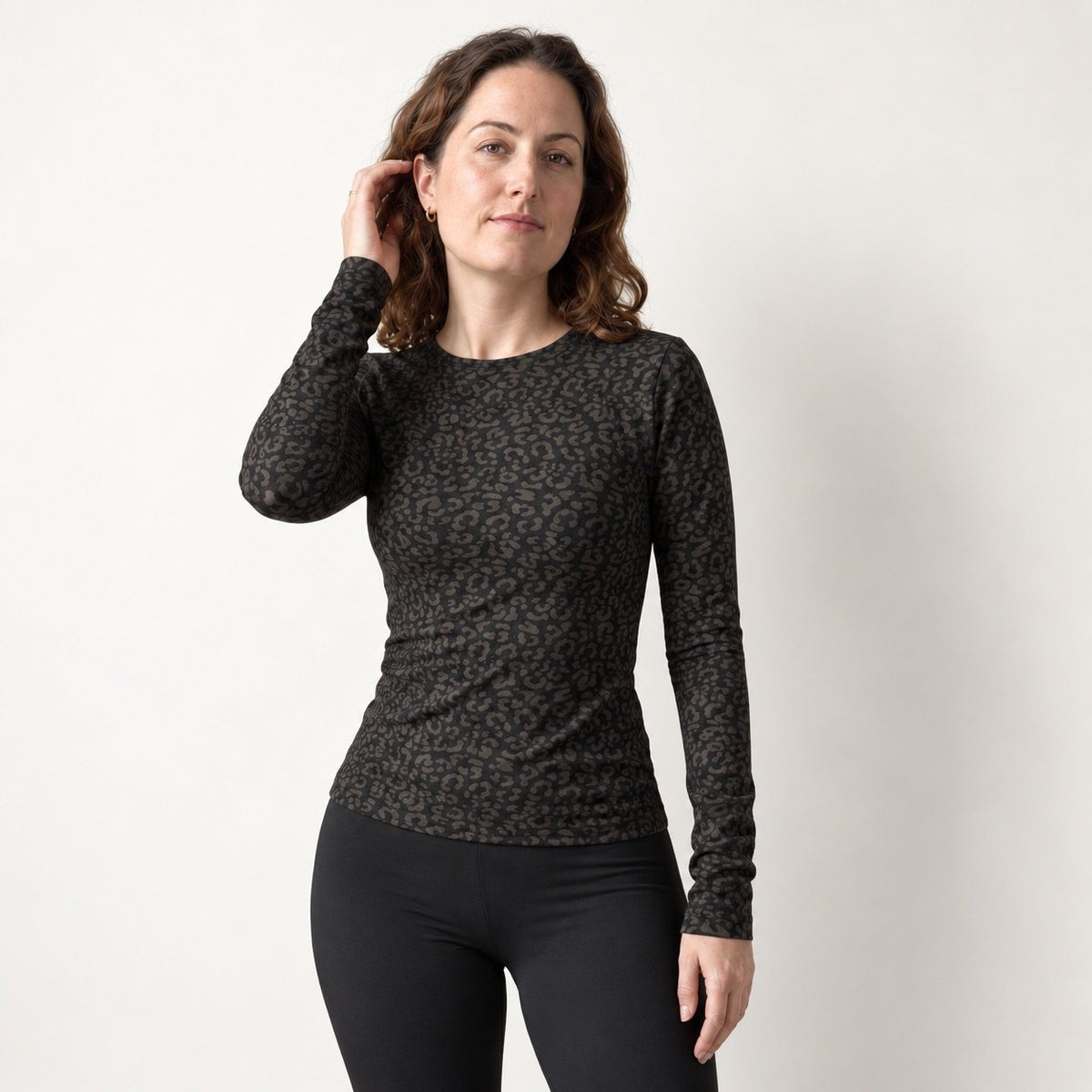 A woman modeling a black leopard long sleeve top with a dark brown and black leopard print pattern, paired with black leggings, against a plain off-white background.