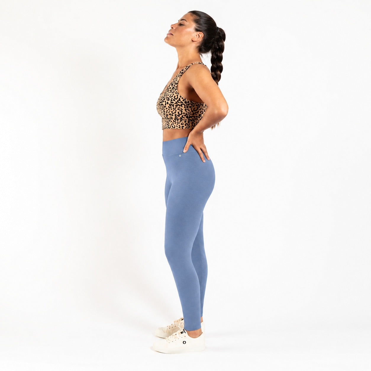 A woman in side profile wearing a leopard-print sports bra and  organic cotton high waist leggings , standing against a plain white studio background.