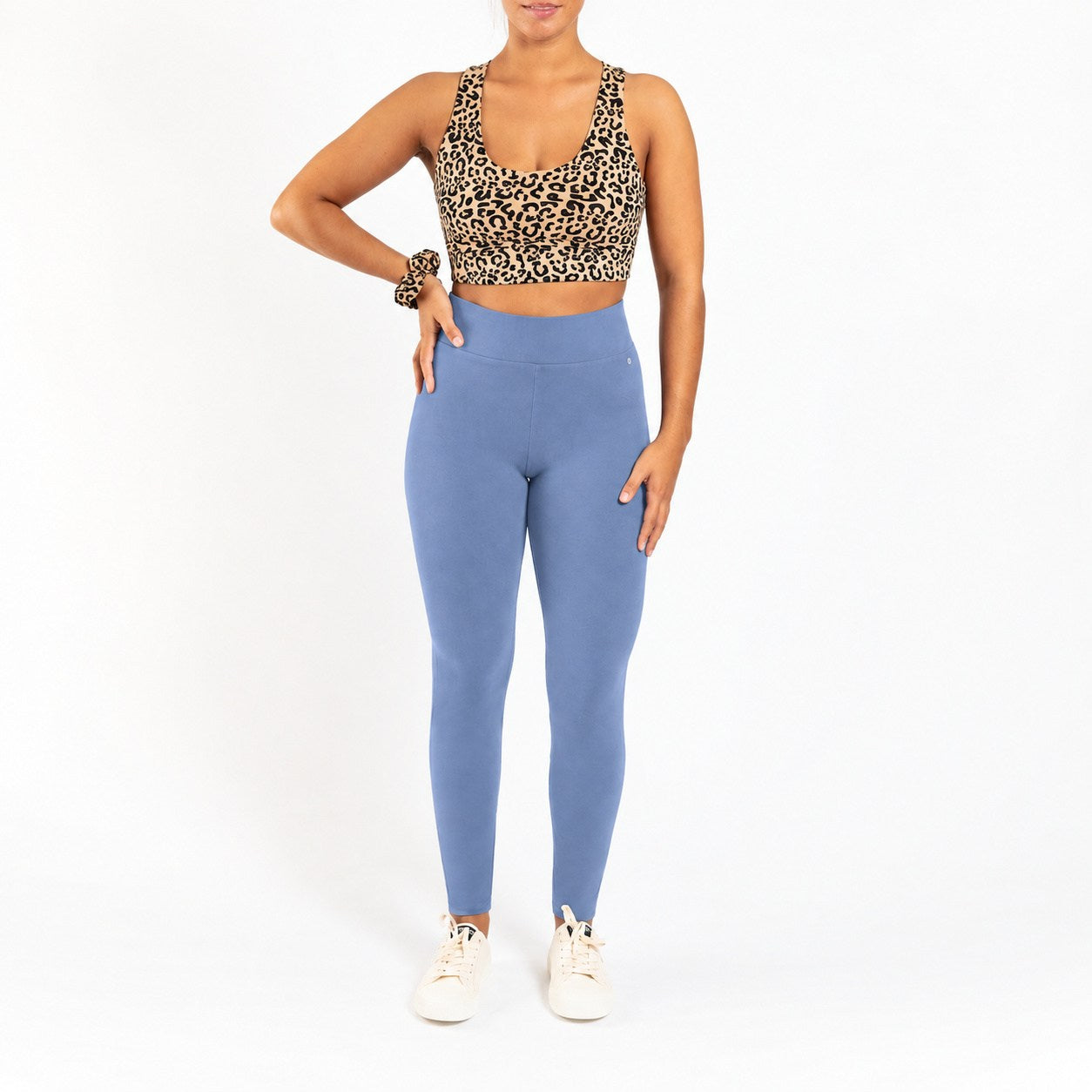 A woman modeling a leopard print sports bra and dusty blue high-waisted leggings against a plain white background.