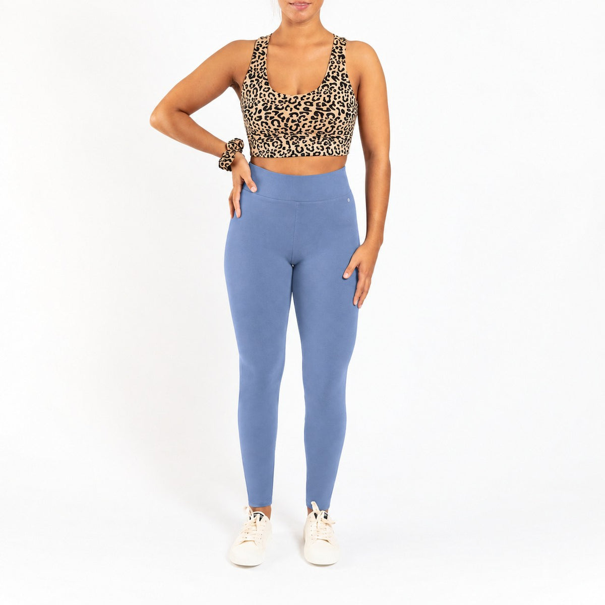 A woman modeling a leopard print sports bra and dusty blue high-waisted leggings against a plain white background.