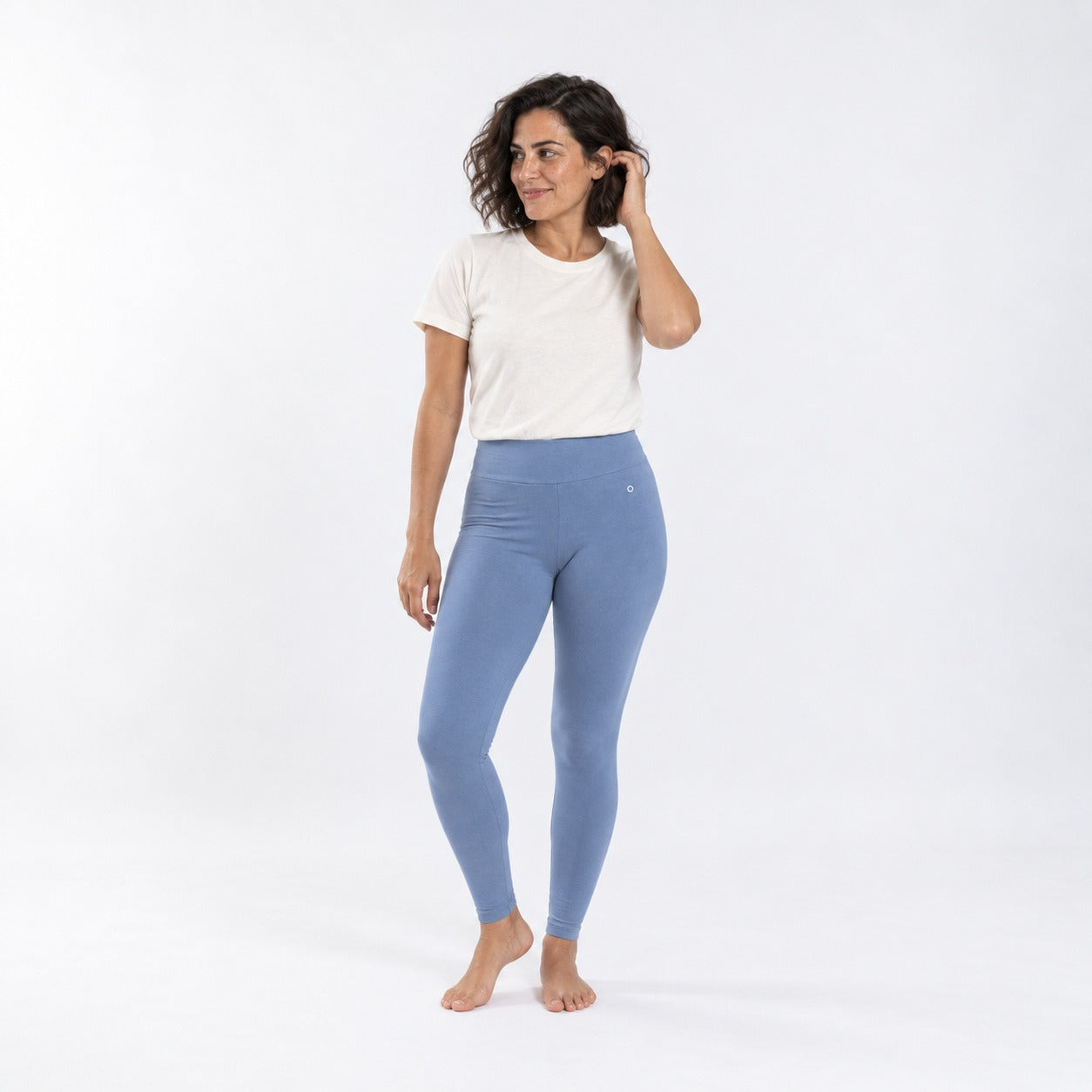 A woman modeling high-waisted, ankle-length blue leggings and a white t-shirt against a plain white studio background.