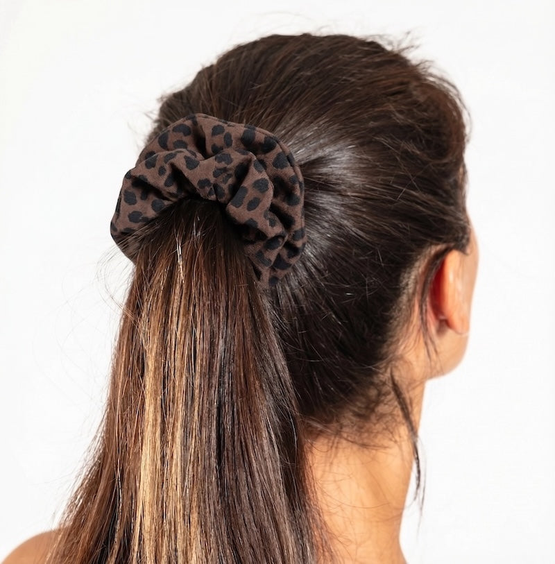 Person with a ponytail holding a leopard print scrunchie against a white background
