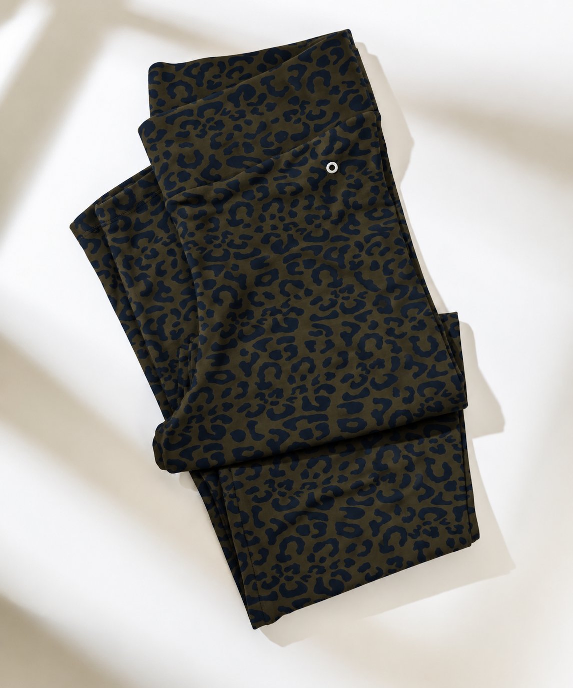 A pair of folded leopard-print leggings in dark olive green and navy blue, displayed on a clean white surface with soft diagonal shadows.