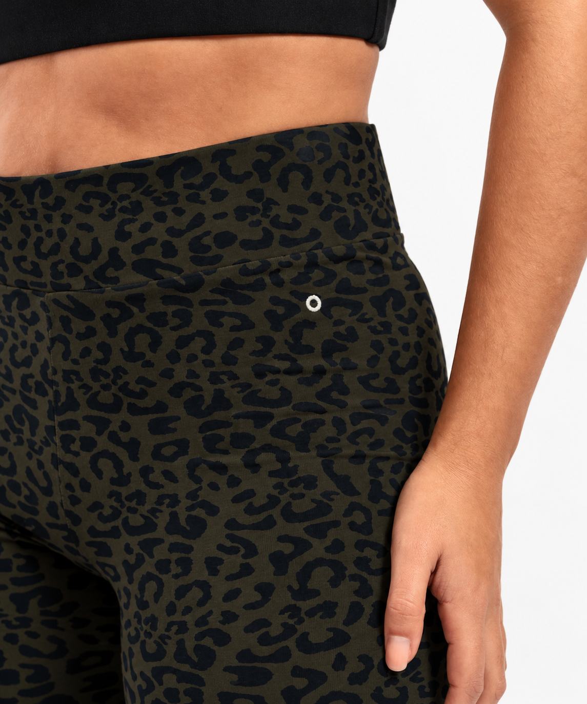 Close-up of a model wearing high-waisted leopard-print leggings in olive green and black, showing the side pocket with a silver grommet.