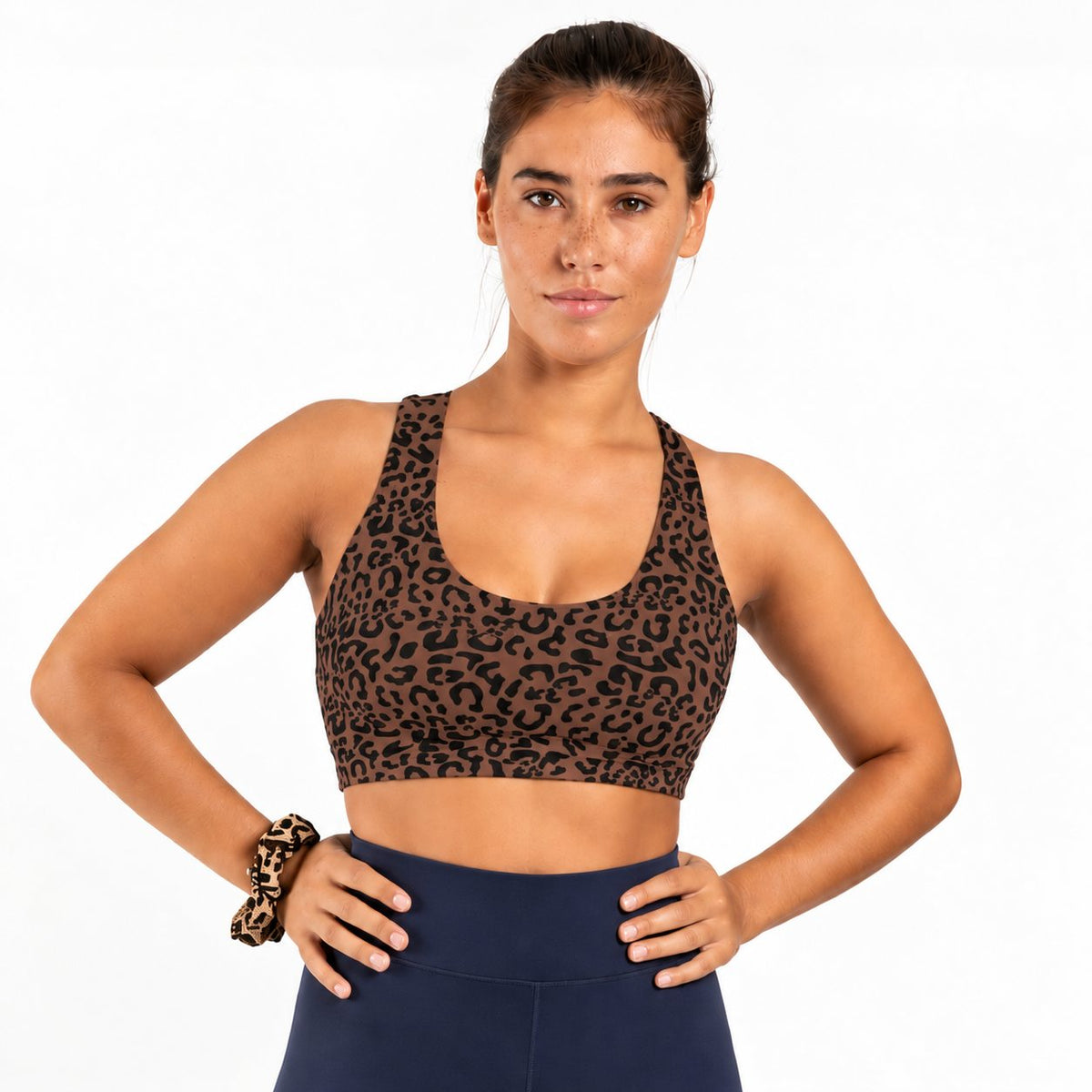 A woman modeling a brown and black leopard print sports bra in soft organic cotton against a plain white background.