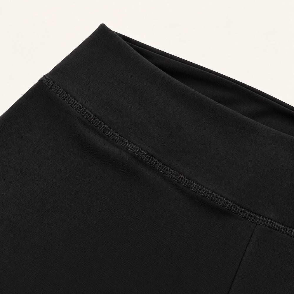 Close-up of a black  organic leggings flared leggings, showing the waistband and upper front panel with a visible seam and ribbed trim against a plain light background.