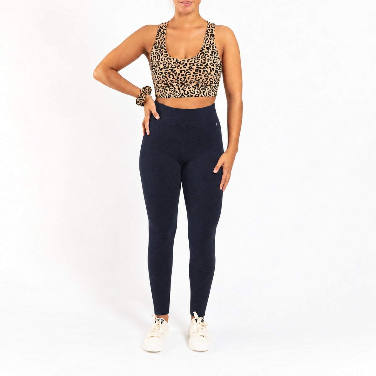 A woman modeling a leopard-print sports bra and organic cotton high waist leggings deep blue color against a plain white background.