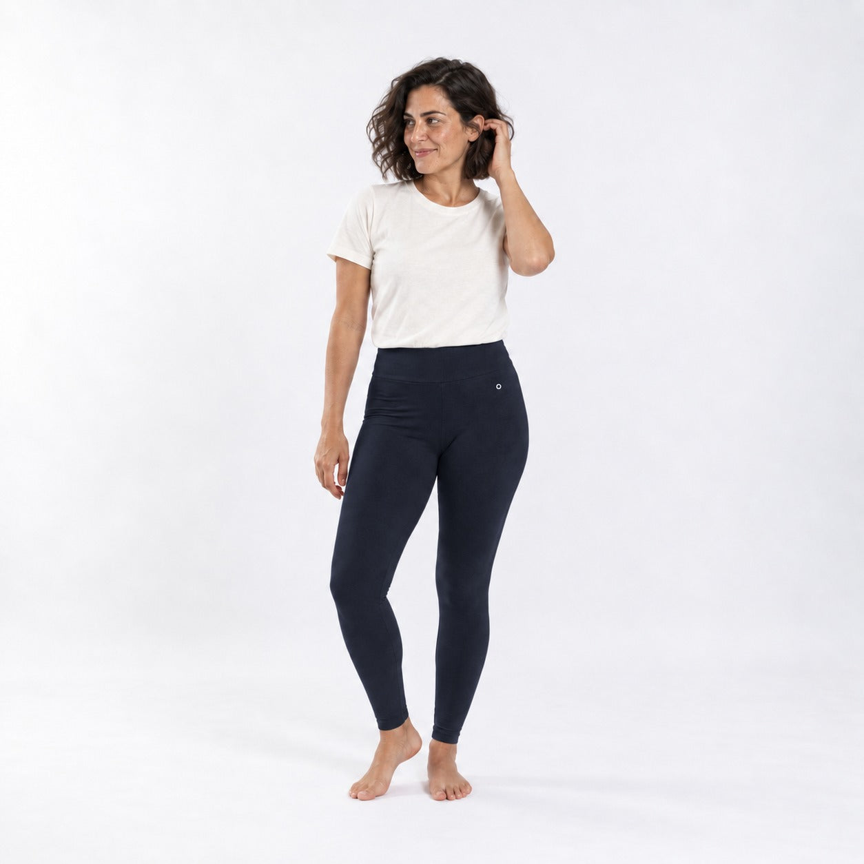 A woman modeling organic cotton high waist leggings deep blue coloand a white t-shirt against a plain white studio background.