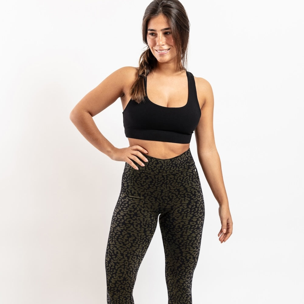 Woman wearing a black sports bra and patterned leggings on a white background