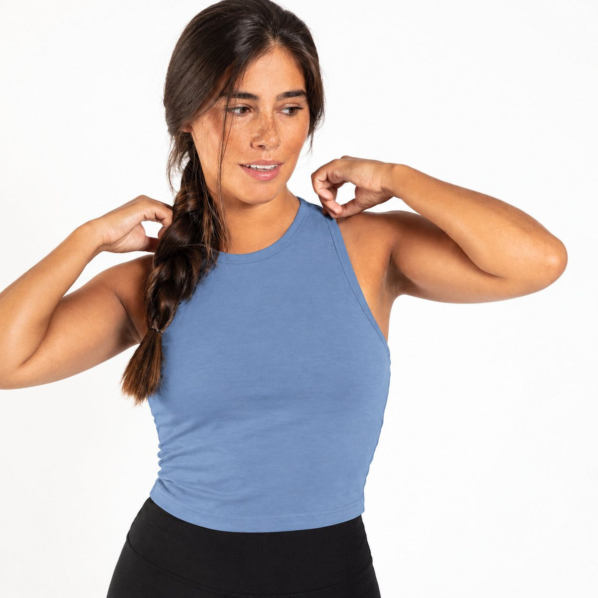 A woman modeling a sleeveless Organic Cotton Tank Top with built in bra in a dusty medium blue color, paired with black leggings, against a solid white background.