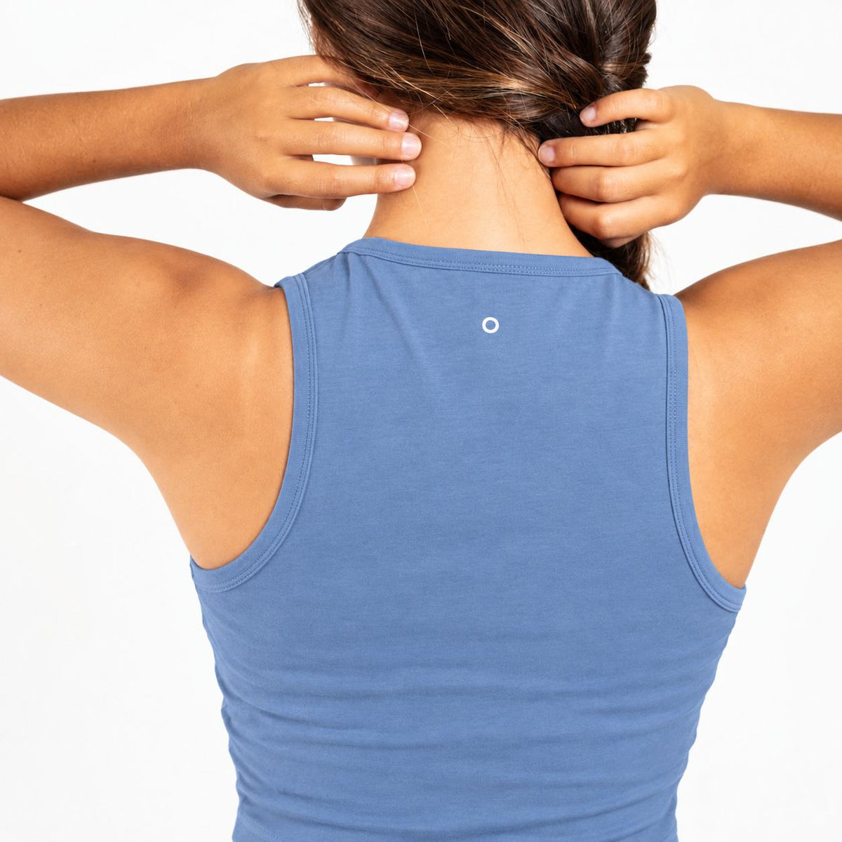 Back view of a woman wearing a heathered blue  Organic Cotton Tank Top with built in bra , adjusting her hair with both hands against a plain white background.